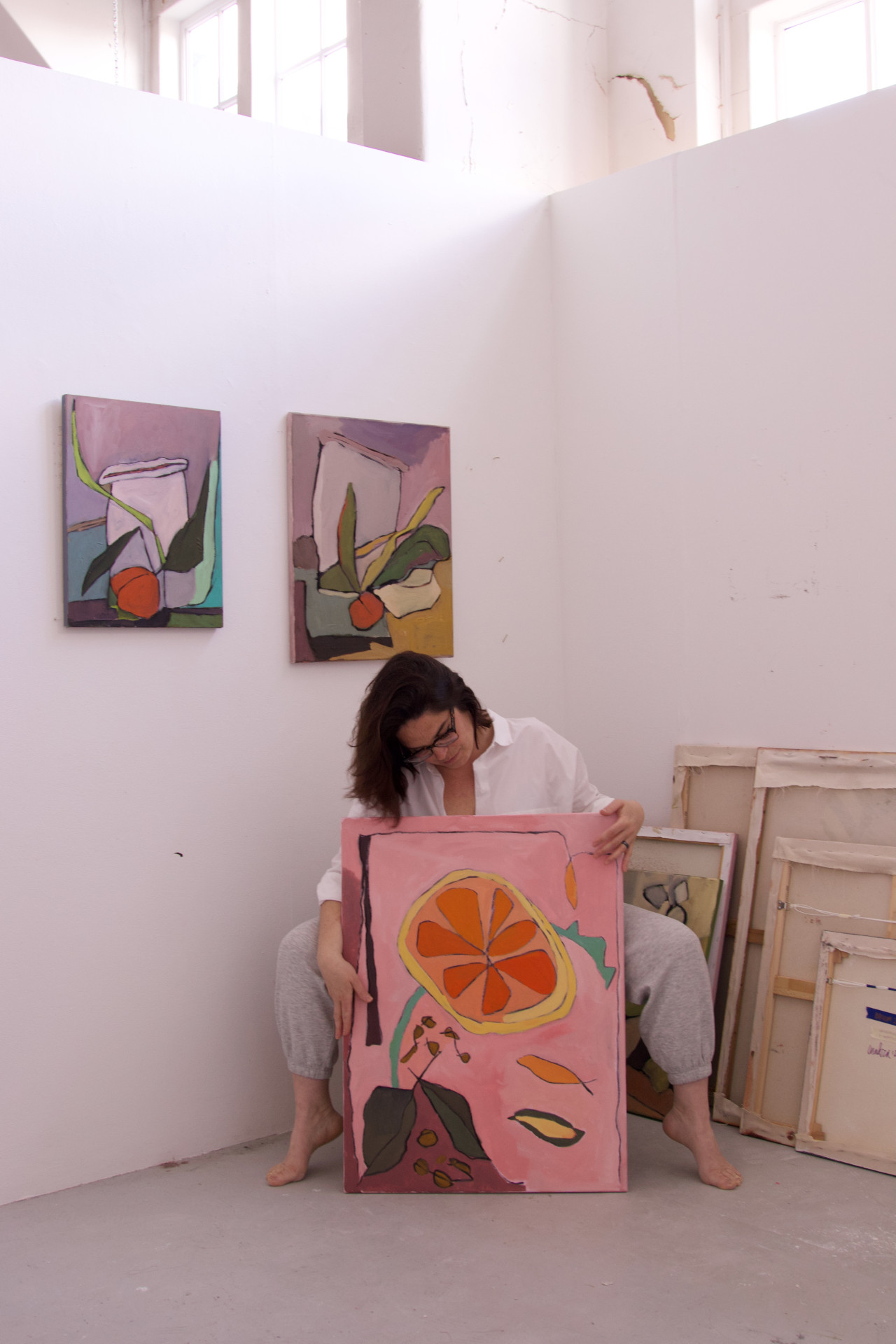 Jessie Cuadra holding painting of flower in gallery beneath two more of her paintings
