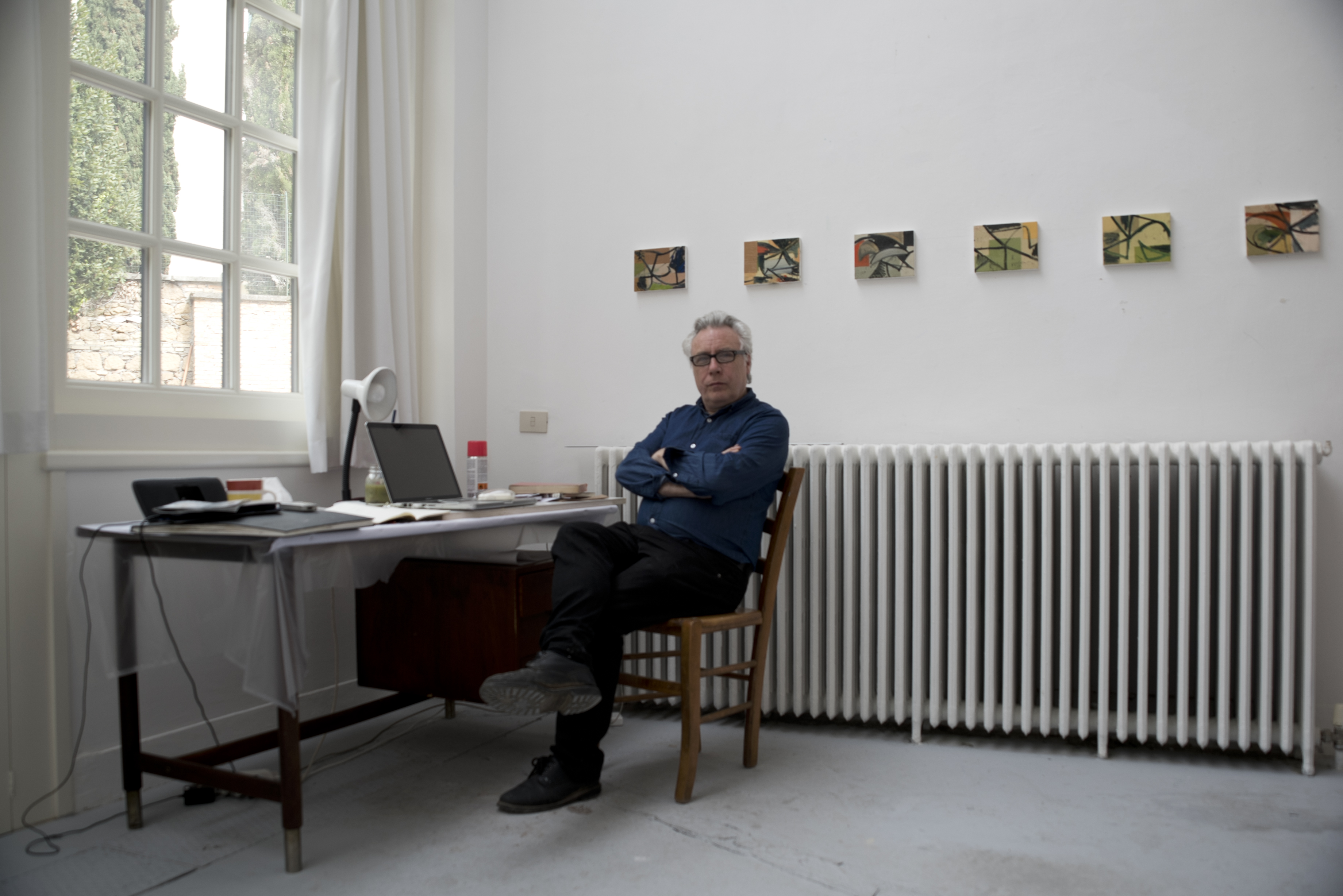 David Ryan sitting at a desk in front of his paintings