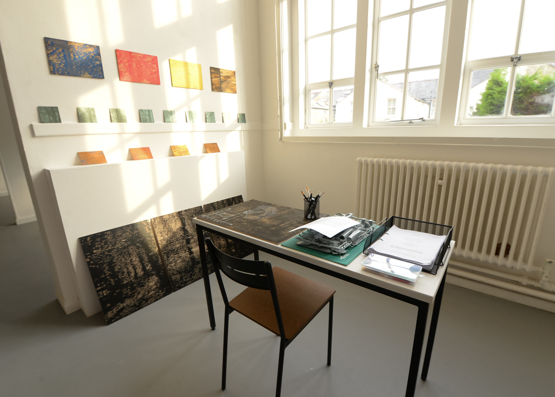Art exhibit featuring chair, desk and paperwork on display in studio