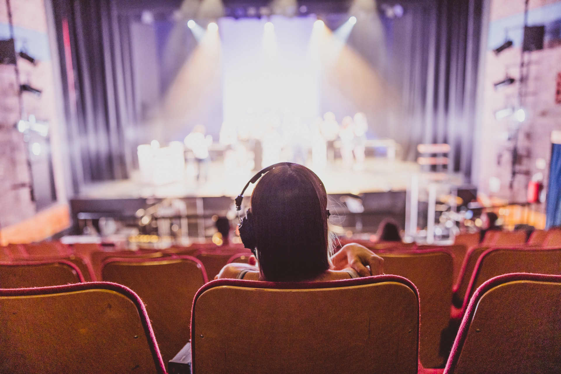 Female student wearing headphones watching performance on stage