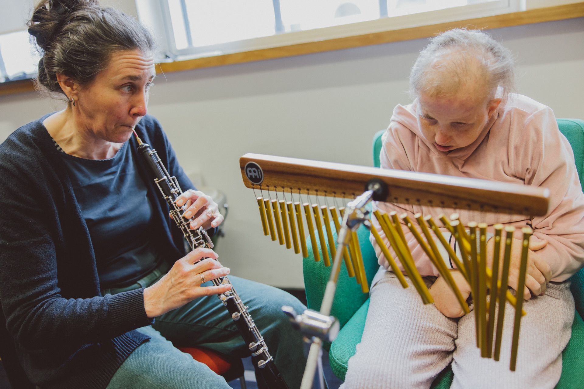 Female music therapist playing oboe with client playing chimes