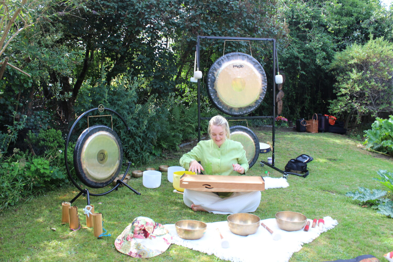 Claire White playing a monochord in garden surrounded by gongs, bowls and candles