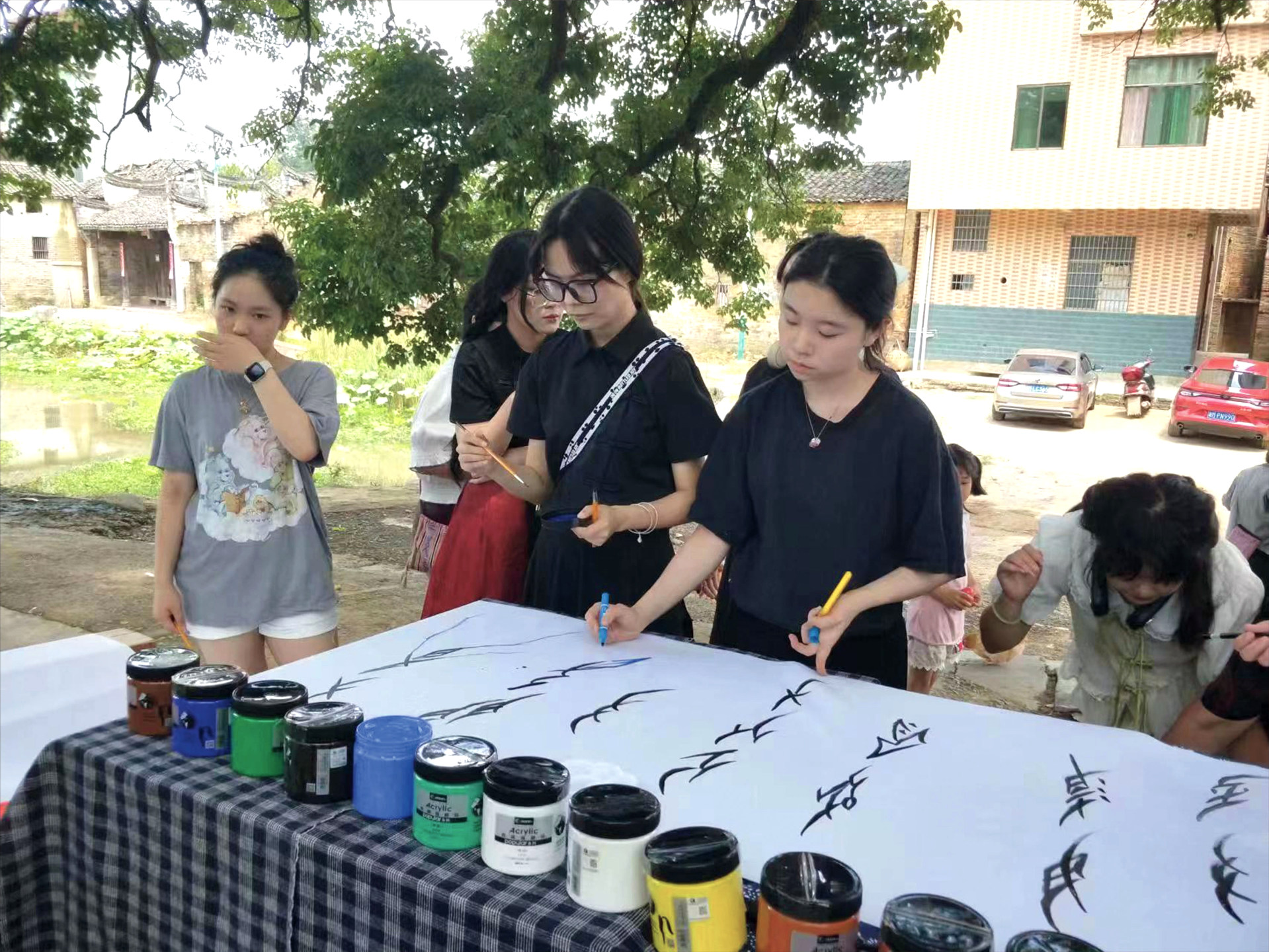 Women painting Chinese characters on long paper strip outside