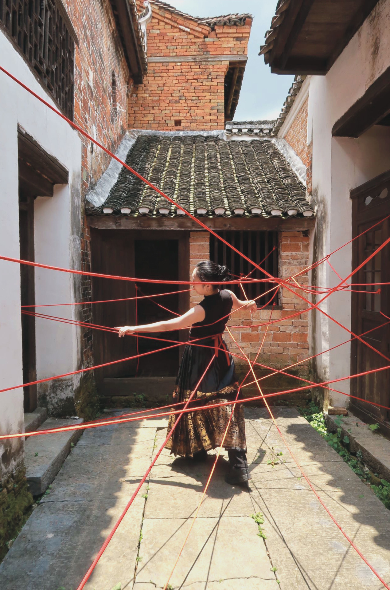 Woman caught in mesh of red threads dancing in small courtyard