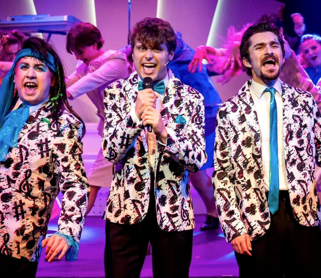 Oliver performing onstage in jazzy suit with two other actors