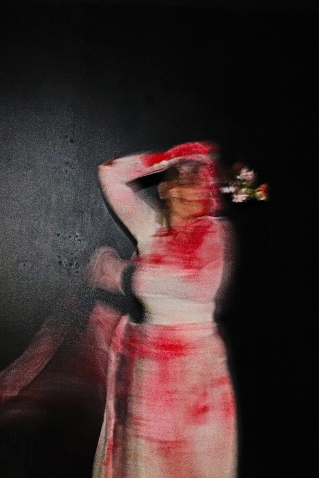 Blurred photo of young woman in white dress covered in red stains holding flowers