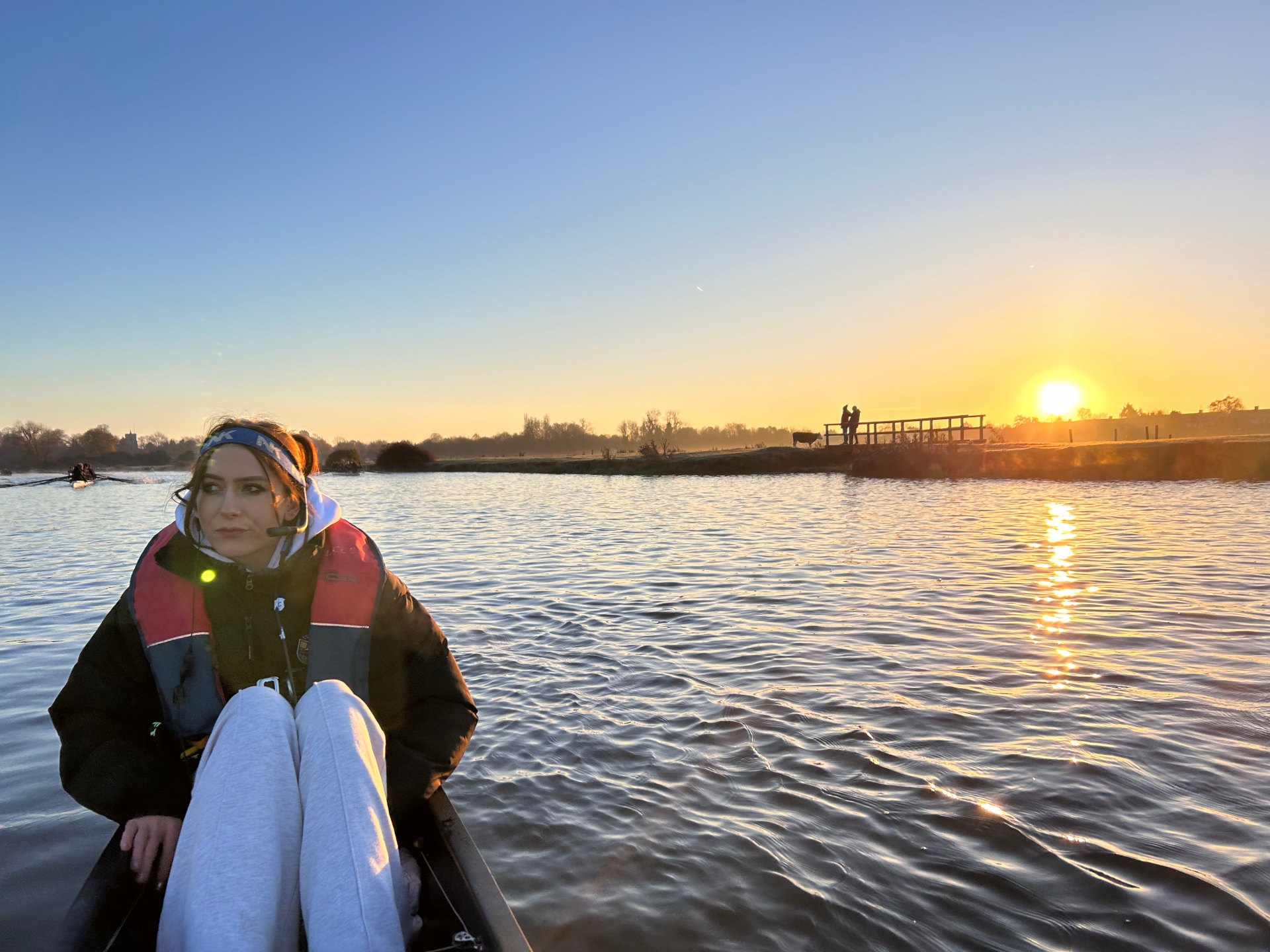Photo of young woman in row boat on river at sunset