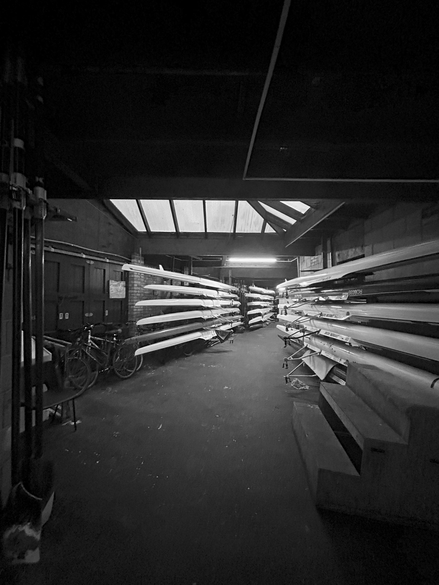 Black-and-white photo of canoes and cycles in shed