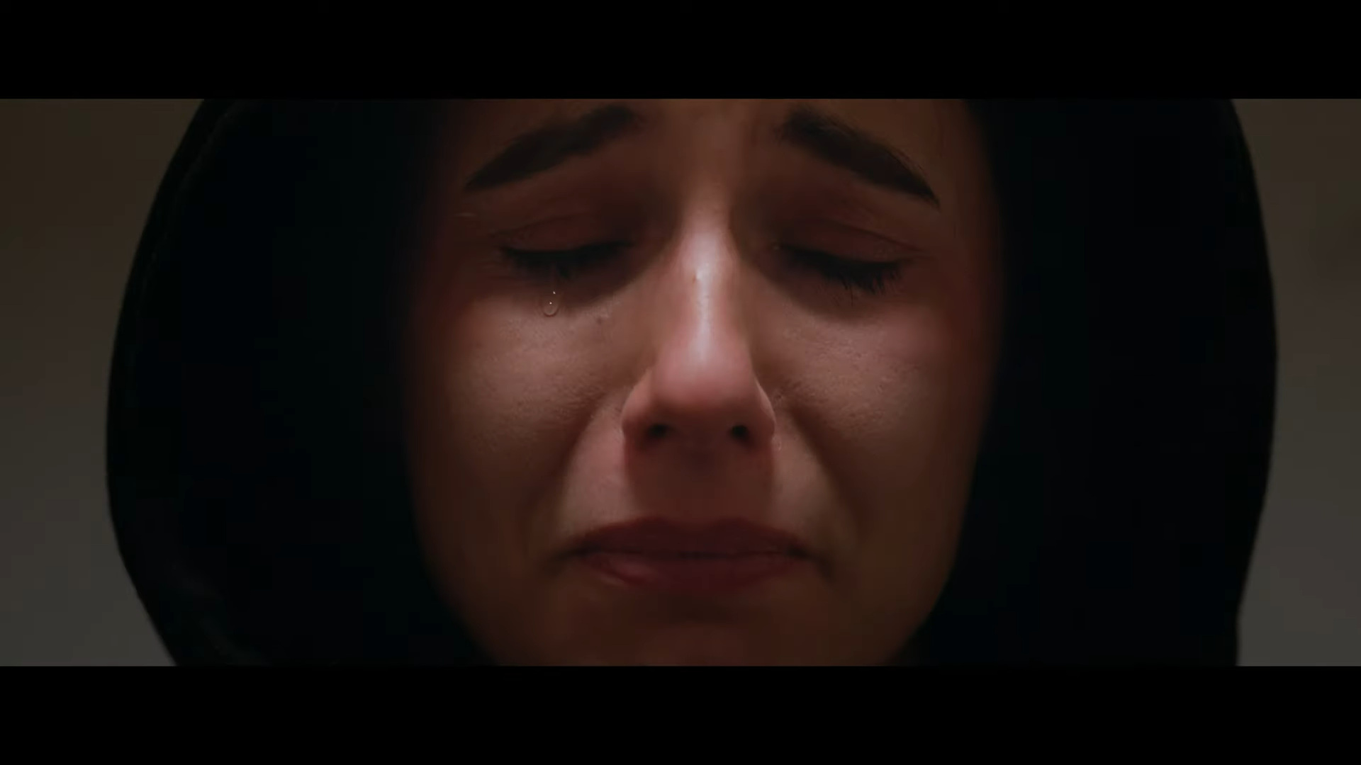 Film still of woman in hoodie crying