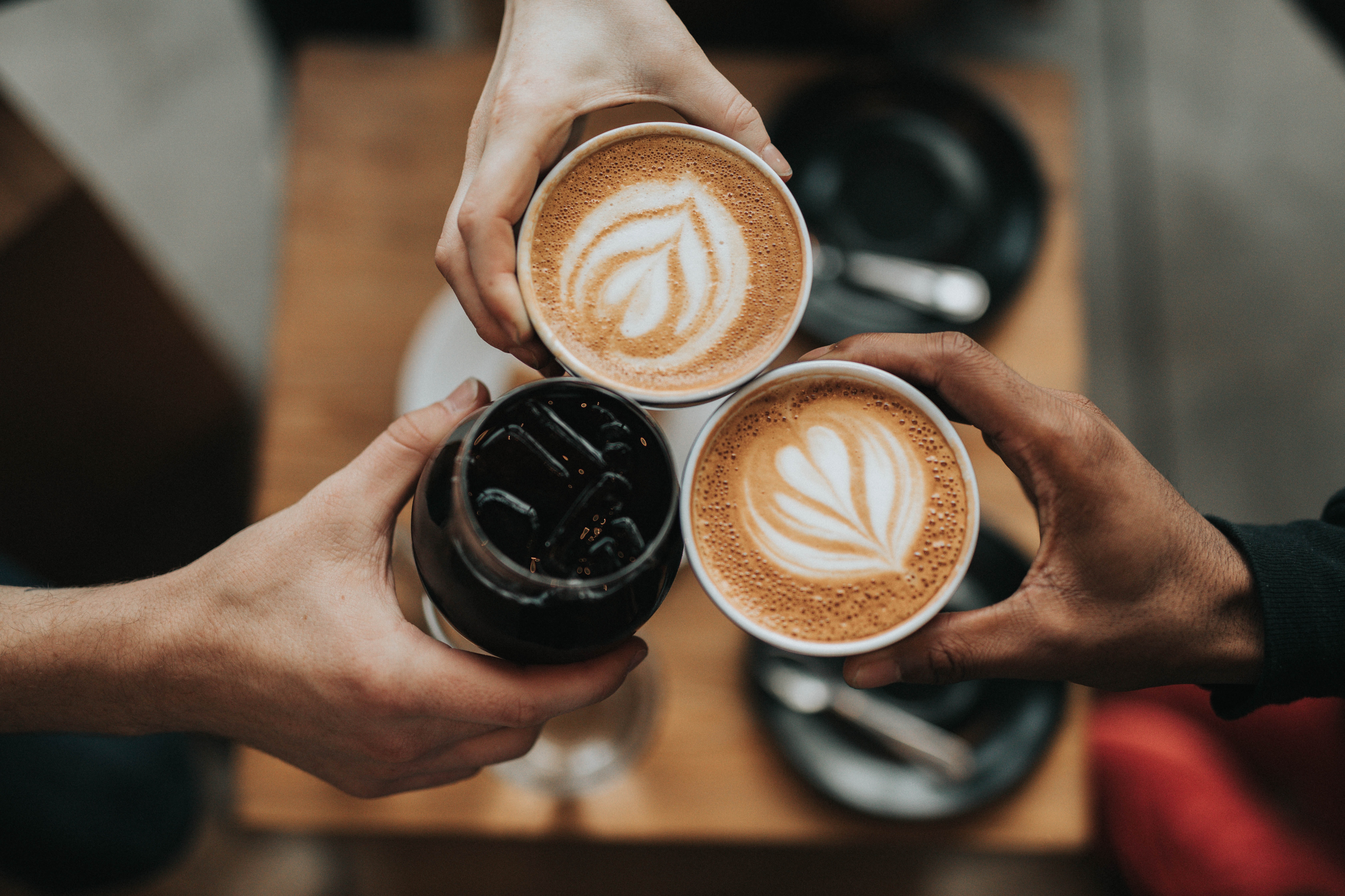 A photo of three hands holding a coffee.