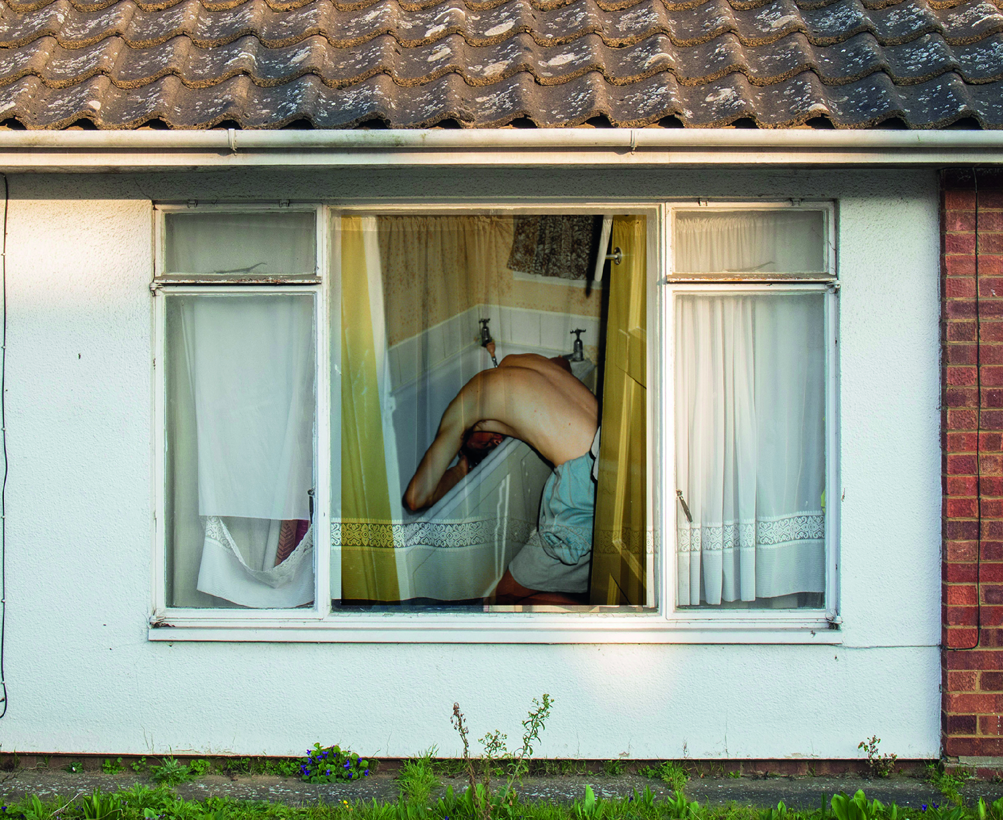 Photo of man washing hair in bath taken through window of house