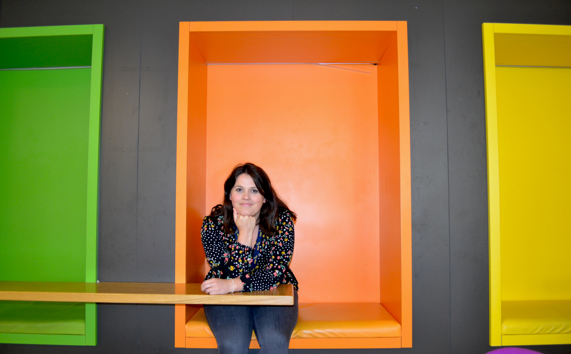 Megan Herdson sitting at a table in front of large coloured cubby holes