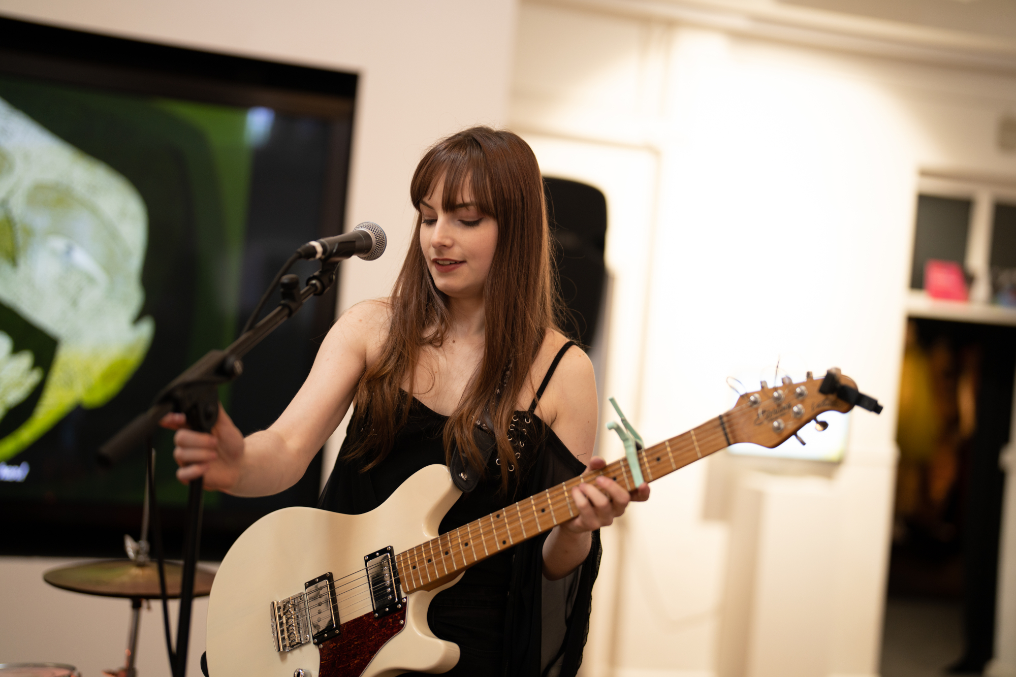 A young woman holding guitar and adjusting mic stand