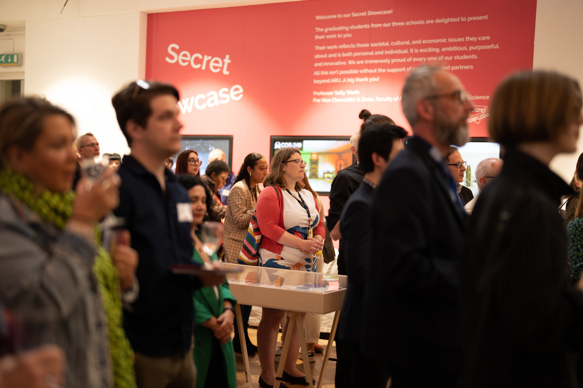 Visitors watching talks beneath a large Secret Showcase poster