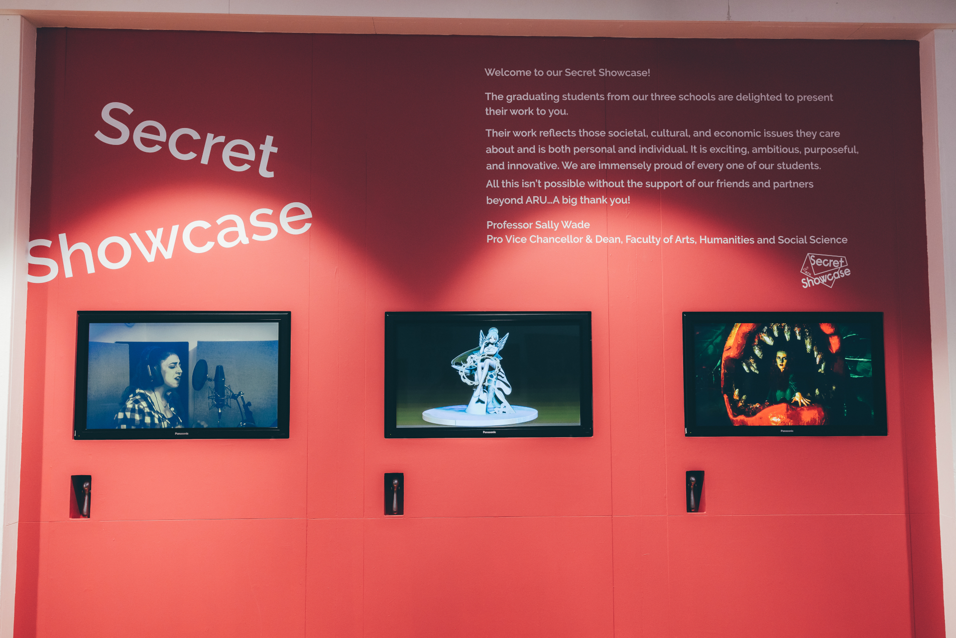 Three video screens embedded into red wall below Secret Showcase title and intro text