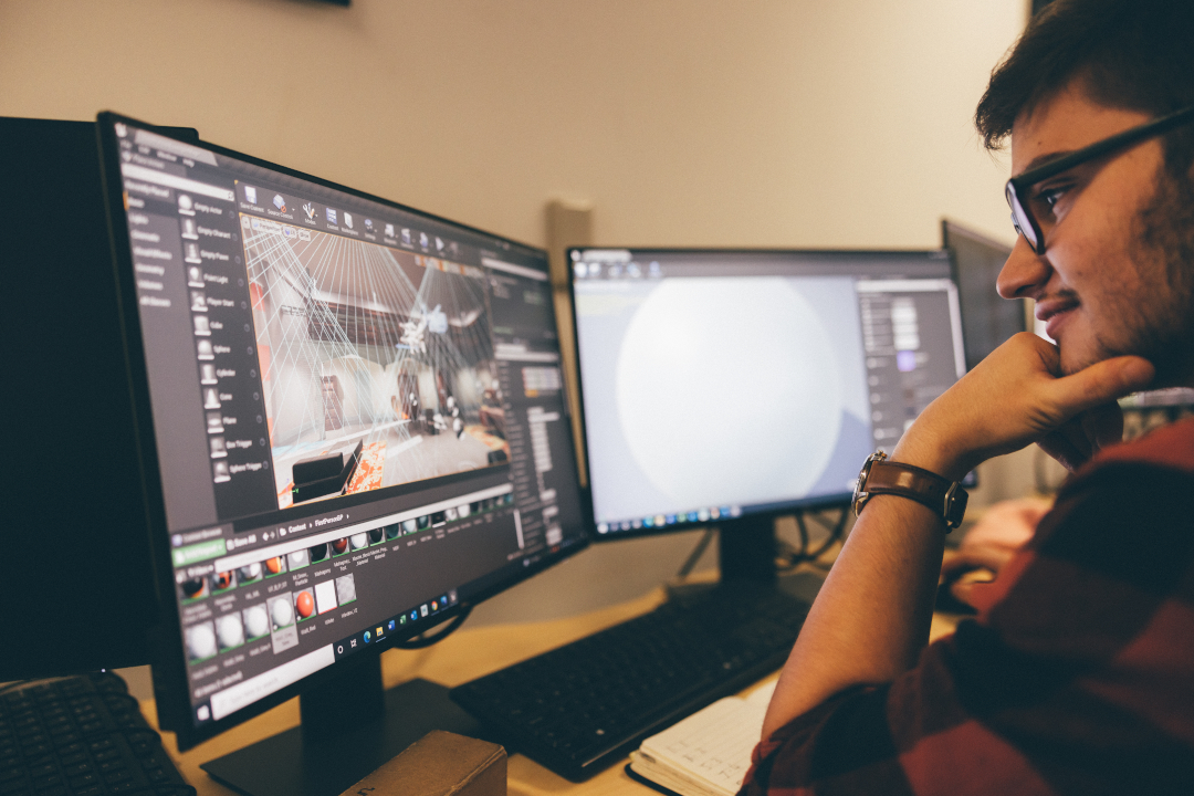 Young man using games design package on dual monitors