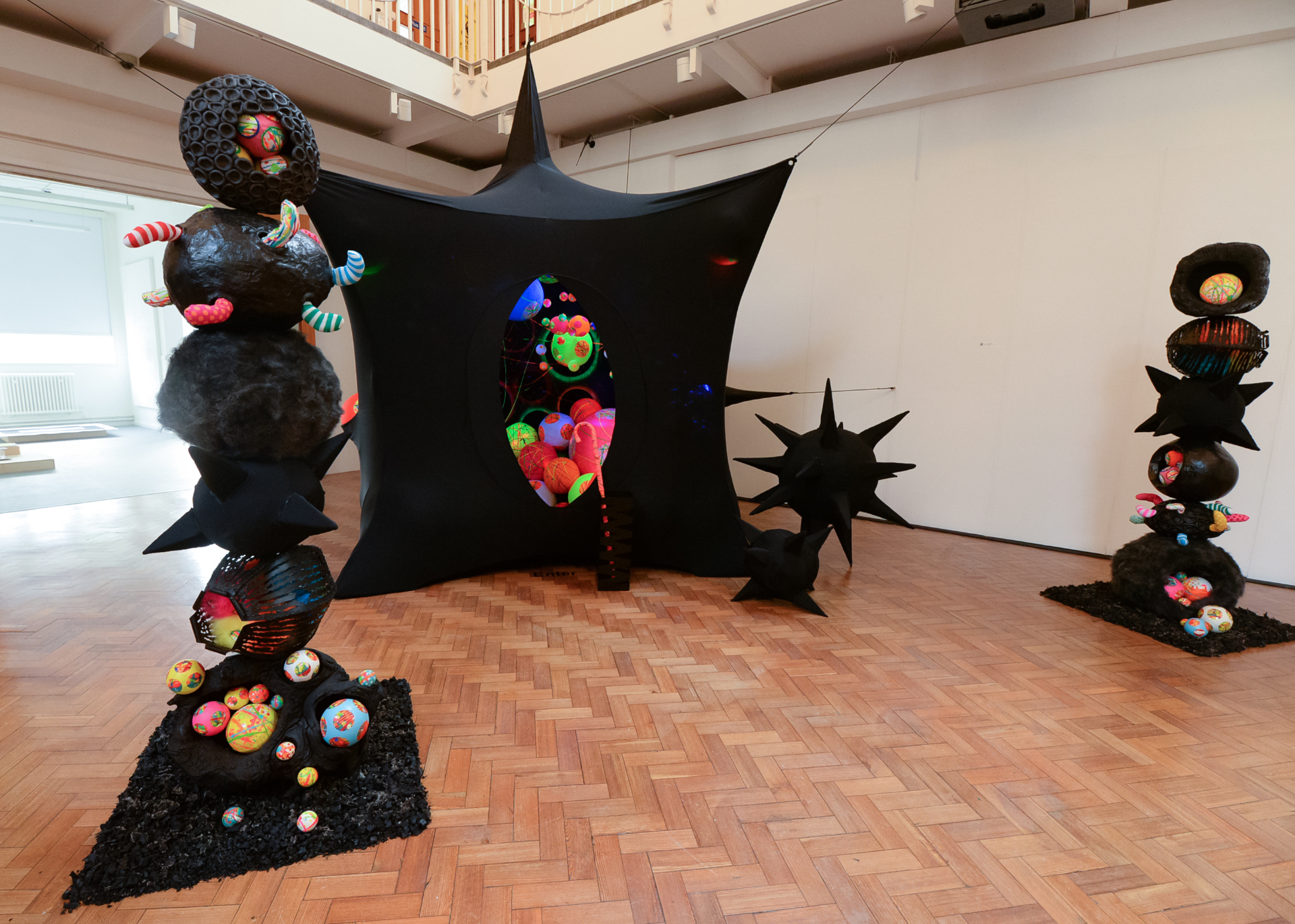 Black spikey tent filled with coloured spheres between two ball-and-spike sculptures in Ruskin Gallery