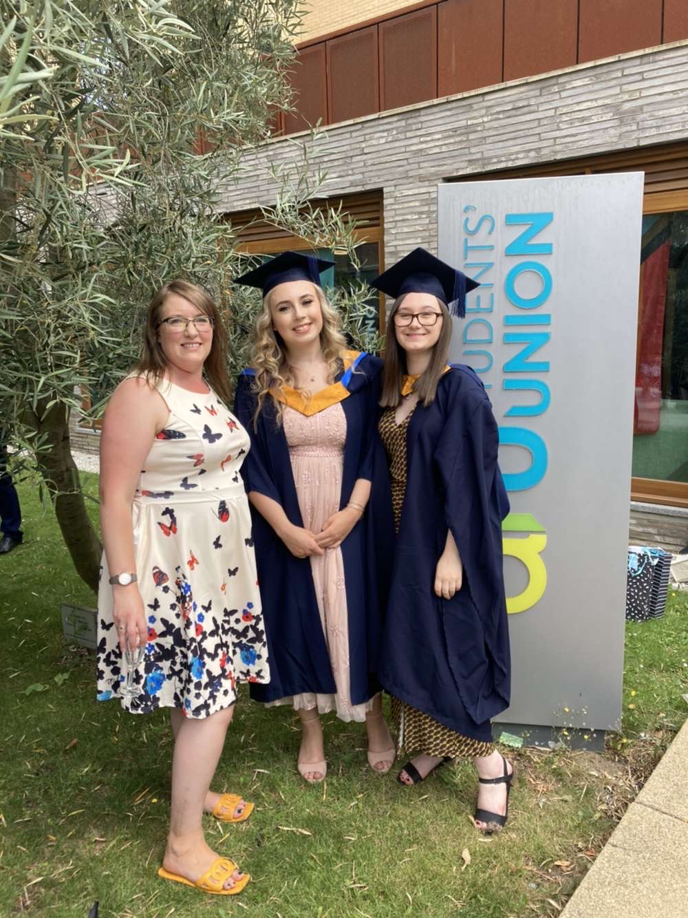 Three women, two wearing graduation gowns