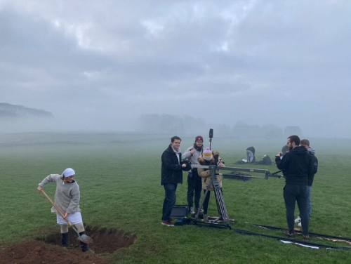 Camera crew in field next to actor digging grave