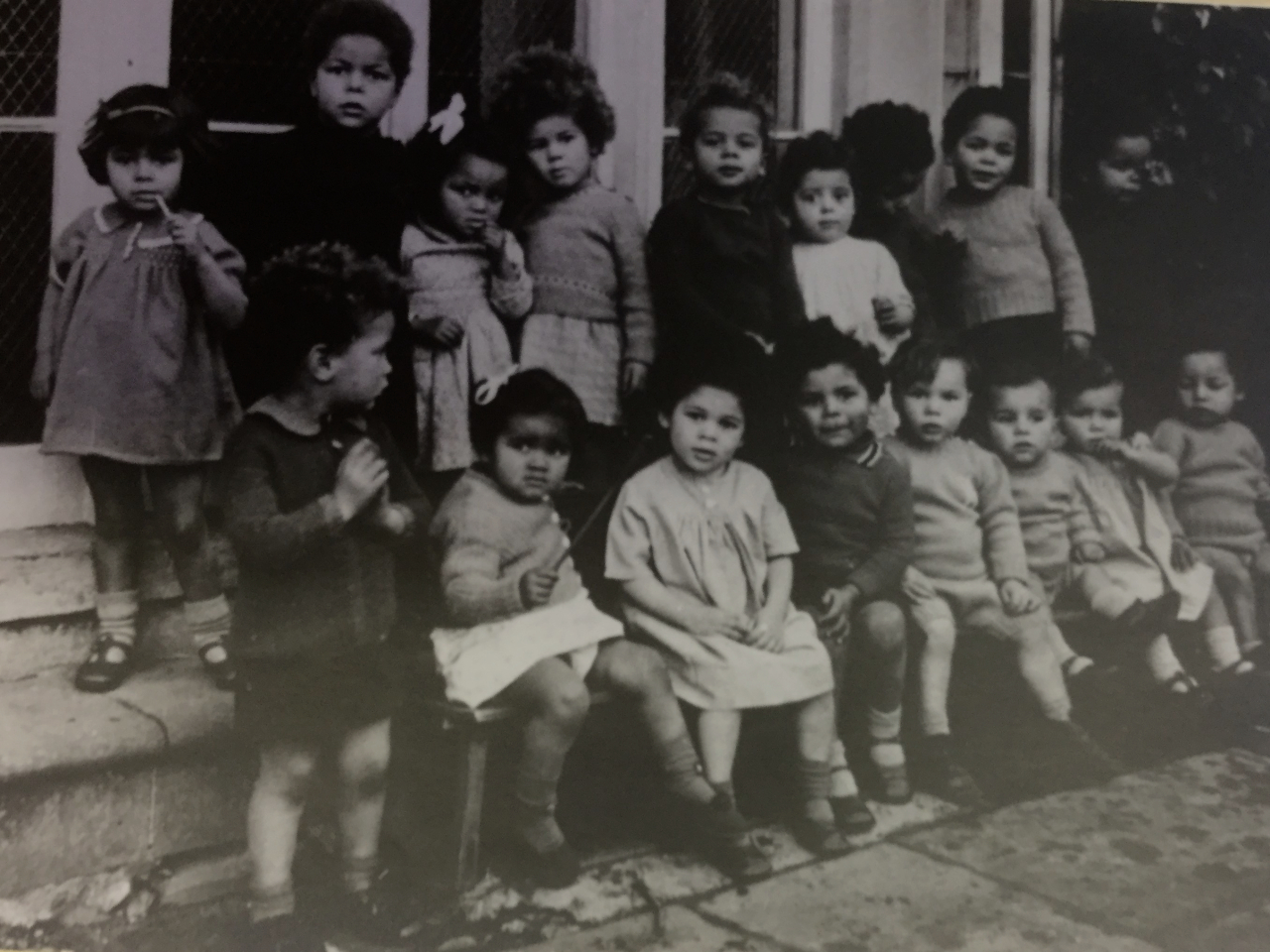 black and white photo of children sitting and standing on steps outside building